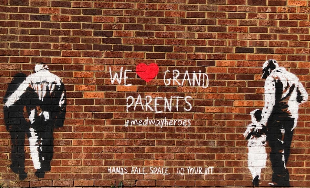 'We heart grand parents' shows a granddaughter helping her grandfather and a father looking after his daughter.  Both images are black and white on an orange brick wall. In-between the two images it reads 'We heart grand parents' #medwayheroes Hands. Face. Space. Do your bit. 