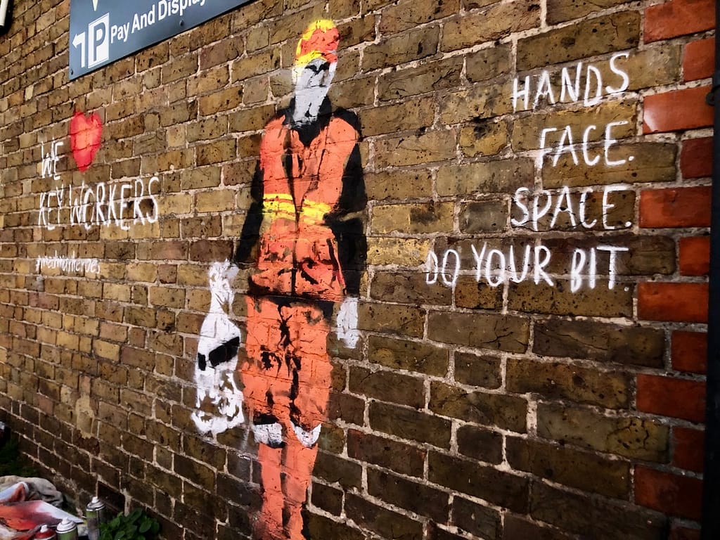 'We Heart Keyworkers' depicts a waste collector in orange, yellow, red, black and grey outfit carrying a white bin bag on a brick wall. It reads 'We heart key workers' #medwayheroes to the left and Hands. Face. Space. Do your bit. to the right 