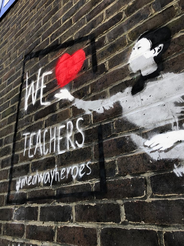 'We Heart Teachers' shows a teacher in a grey jumper and black hair pointing her right arm towards a black framed board. The red heart comes of her hand and it reads 'We heart teachers' #medway heroes.