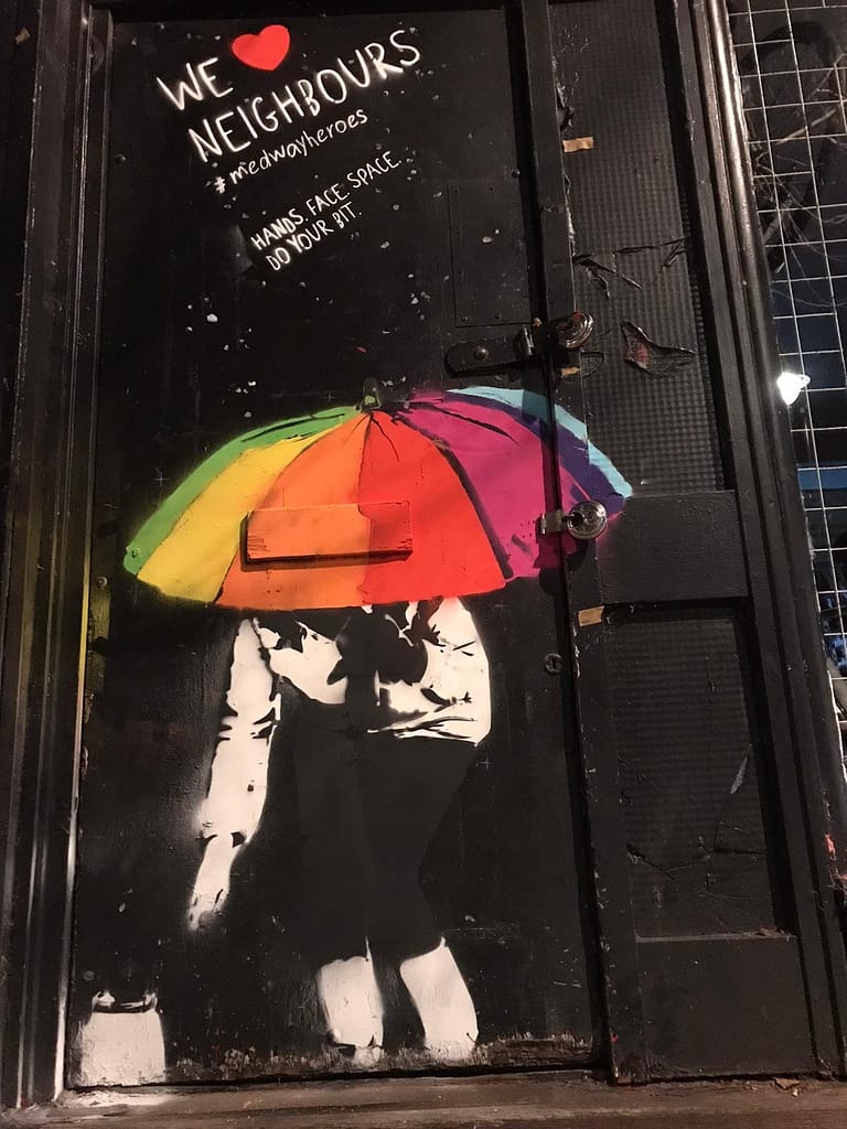 We heart neighbours is showing a woman with a rainbow umbrella on a black door dropping off a jar of food. It says We heart neighbours. #medwayheroes. Hands. Face. Space. Do your bit