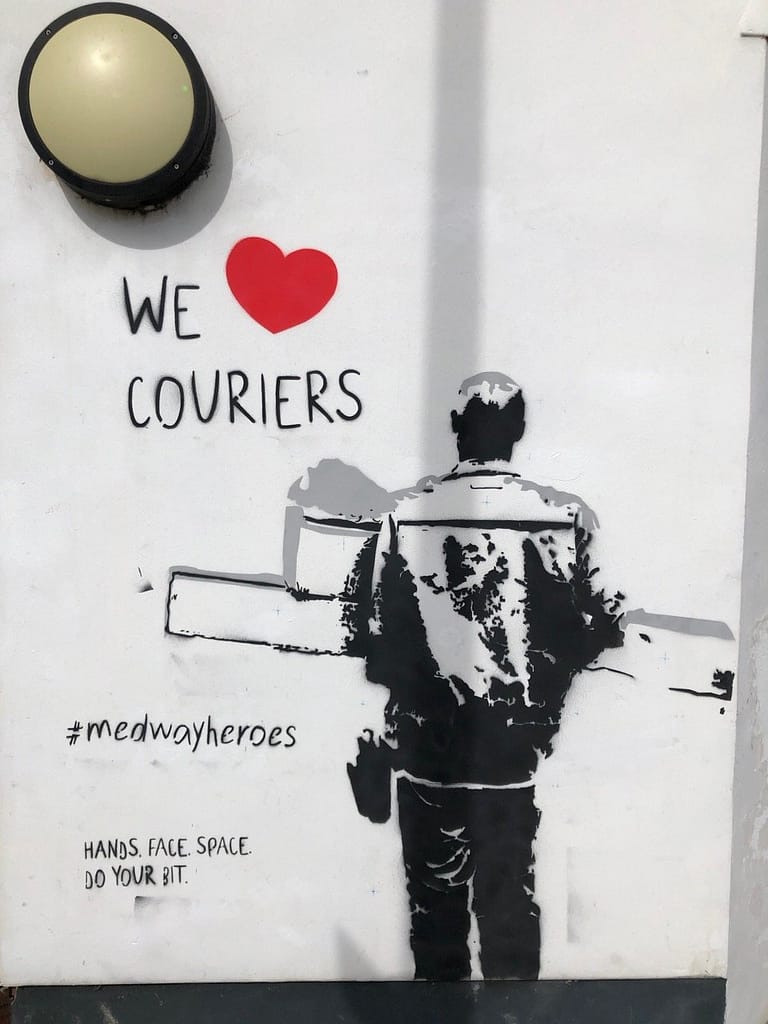 'We Heart Couriers' shows a courier in black and grey from behind delivering boxes. It says 'we heart couriers' above to the left and #medwayheroes to the left as well as 'Hands. Face. Space. Do your bit.' It's on a white wall of the Strood Community Hub