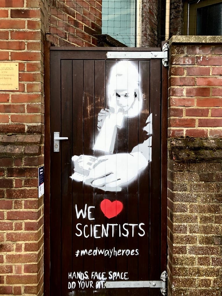 'We Heart Scientists' shows a scientist in full protective gear looking through magnifying equipment. The figure is appearing out of a door. It reads 'We Heart Scientists' Hands. Face 
