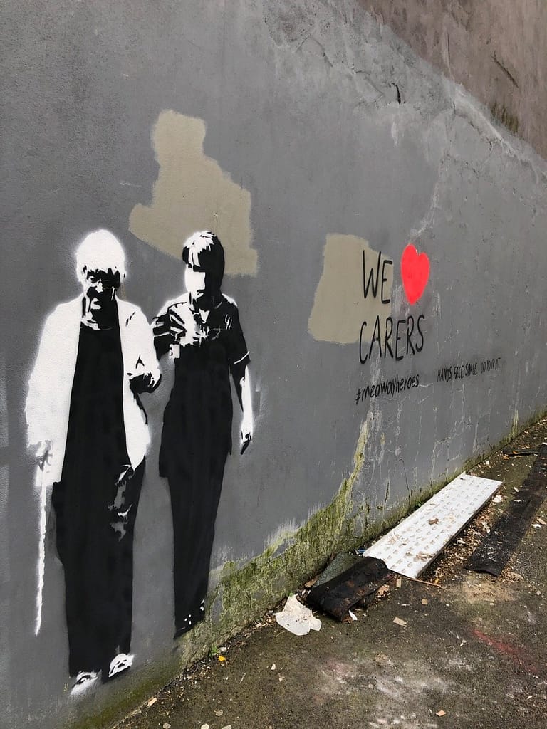'We heart carers' shows an old lady walking with her walking stick supported by a kind masked carer. Both are in black and white. It reads 'We heart carers' to the right